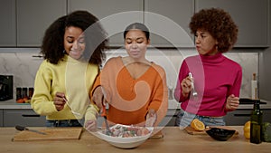 Positive African American women tasting fresh delicious vegetable salad
