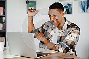 Positive african man gesturing while having video call via laptop at home