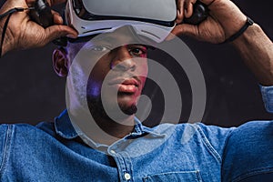 Positive african man taking off his VR glasses from his head on black background
