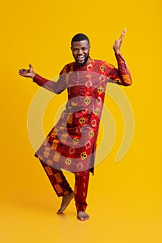 Positive african man in traditional dress dancing over yellow