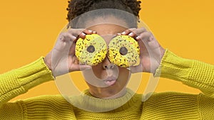 Positive afro-american woman holding donuts front of eyes, playful mood, joking