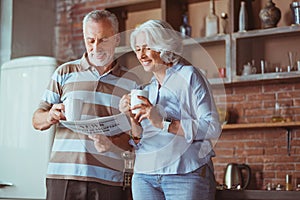 Positive aged couple reading daily press in the kitchen