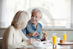 Positive aged spouses eating breakfast talking sitting in the kitchen photo