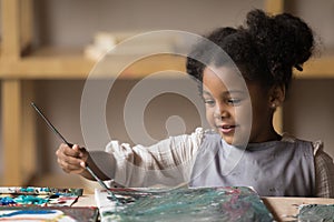 Positive art school African pupil girl in apron enjoying painting