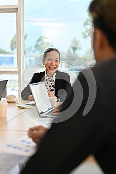 Positive Asian aged female boss or executive manager talking with male financial analysts