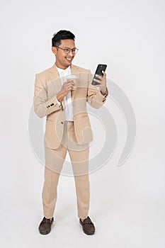 A positive Asian businessman is using his phone and walking with a coffee cup in his hand