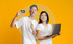 Positive asian couple recommending credit card for shopping online