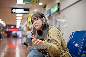 A positive Asian female traveler is talking on the phone while waiting her friend at the airport