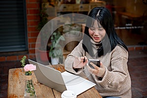 A positive Asian woman is checking messages on her phone while sitting at a table in a cafe