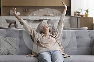 Positive awaking mature woman sitting on comfortable sofa photo