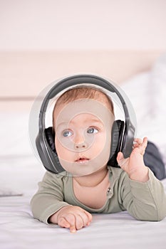 positive baby lying on a white background in headphones listening to music, infant 3 months old with headphones, young