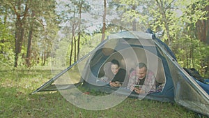 Positive backpacker couple on camping trip using cellphones in tent