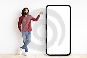 Positive bearded indian guy pointing at smartphone with white screen
