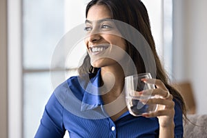 Positive beautiful 20s Indian girl holding glass of clear water