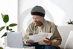 Positive black guy with laptop studying online at home, writing coursework paper or getting ready for exam photo