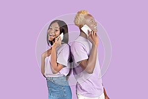 Positive black man and his girlfriend calling on smartphones, having pleasant conversation over lilac studio background