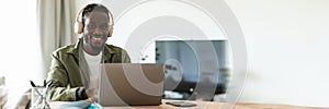 Positive black man in wireless headphones working online on laptop