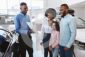 Positive black salesman offering Afro family to sign auto purchase or rental agreement at dealership