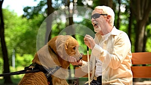 Positive blind man feeding guide dog, sitting in park, nutritious canine food