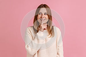 Positive blond woman standing, showing hush sign and looking away, sharing secret.