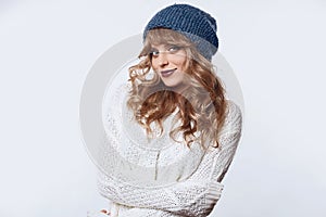 Positive blond woman in sweater and hat on white background