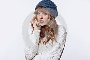 Positive blond woman in sweater and hat on white background