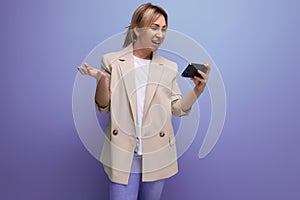 positive blond young woman in a jacket is versed in the new technology of a smartphone on a studio background photo