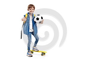 Positive blonde boy with skateboard and backpack holding soccer ball on white background. Back to School.