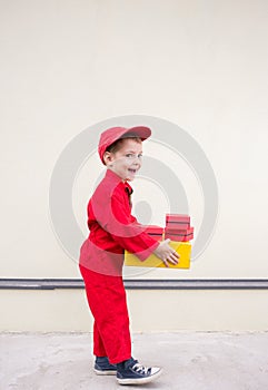 positive boy 3-4 years old in a red uniform and cap with a cardboard box in his hands