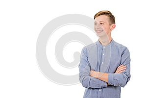 Positive boy adolescent keeps arms crossed looking aside tooth smile isolated over white background with copy space.