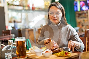 Positive brunette having lunch in cafe with roasted ham hock and beer