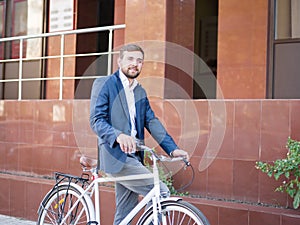 Positive business man with a bicycle on a city background. Eco transport concept. Copy space.