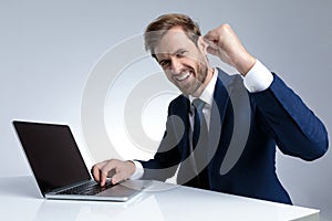 Positive businessman celebrating and writing on his laptop