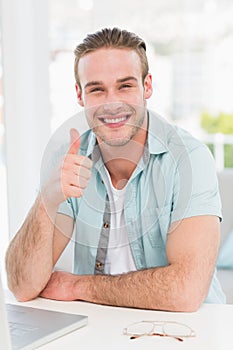 Positive businessman at desk with thumb up