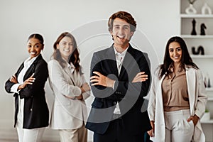 Positive businessman leader standing with folded arms in front of his multiracial female employees, posing in office