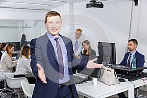 Positive businessman standing in coworking space with open hand