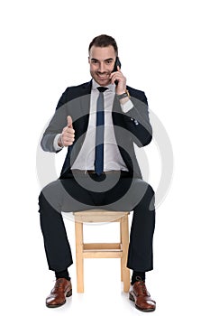 Positive businessman talking on phone and giving thumbs-up, laughing