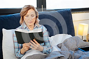 Positive calm woman holding open bible and thoughtfully reading