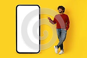 Positive casual indian guy pointing at smartphone with white screen