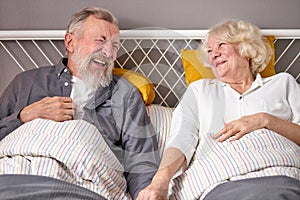 positive caucasian elderly couple have fun. laugh while lying on bed at home