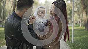 Positive Caucasian parents playing with cute little boy outdoors. Cheerful man and woman enjoying leisure with infant