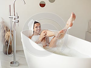 Positive Caucasian woman enjoying hot bath lying in tub at home and laughing in good mood. Pretty young female bathing