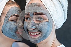 Positive caucasian women wear white towel having fun black clay or mud facial skin mask 