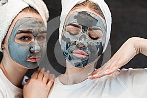 Positive caucasian women wear white towel having fun black clay or mud facial skin mask isolated