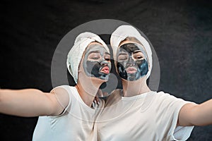 Positive caucasian women wear white towel having fun black clay or mud facial skin mask isolated