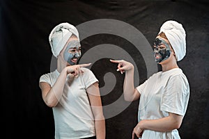 Positive caucasian women wear white towel having fun black clay or mud facial skin mask isolated