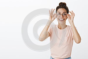 Positive and charismatic good-looking young european female student putting on new transparent glasses smiling broadly