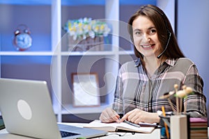 Positive charming woman working at home. Smiling young woman student wear headset using laptop for e learning course