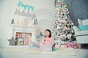 Positive cheerful baby girl sitting with Christmas gift near Christmas tree. Happy New Year