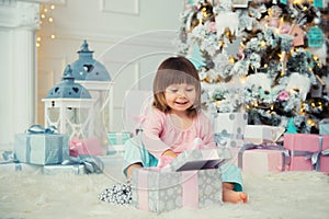 Positive cheerful baby girl sitting with Christmas gift near Christmas tree. Happy New Year